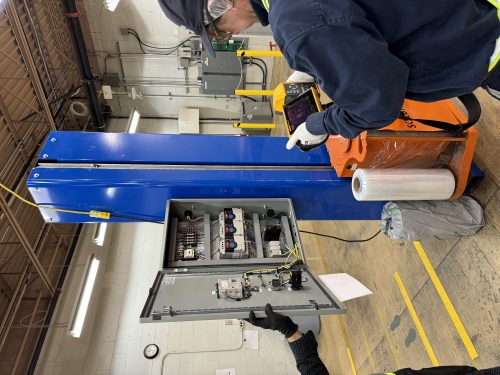 Panneau de contrôle électrique industriel ouvert près d'une machine d'emballage bleue