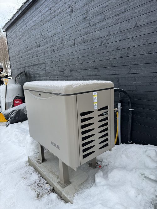 Génératrice Kohler installée à l'extérieur d'une résidence au revêtement noir, en hiver