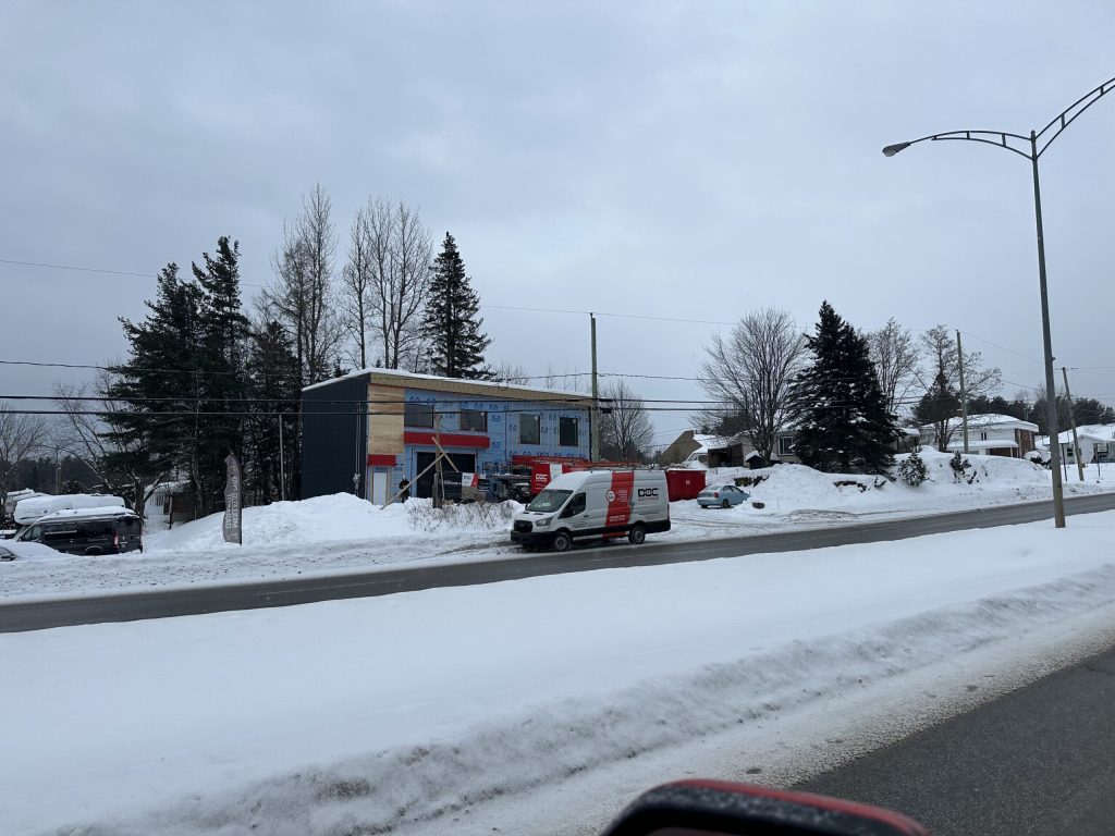 Bâtiment en construction avec pare-air bleu et fourgon de service Doc Électrique, en hiver