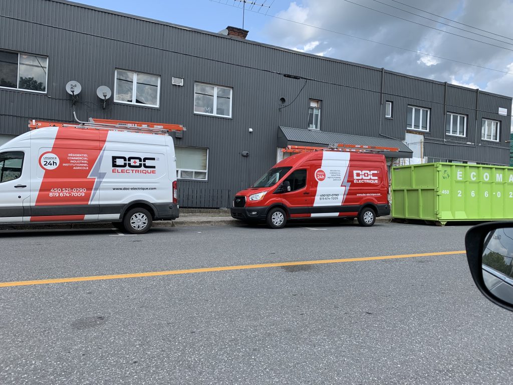 Véhicules Doc Électrique stationnés devant un bâtiment industriel