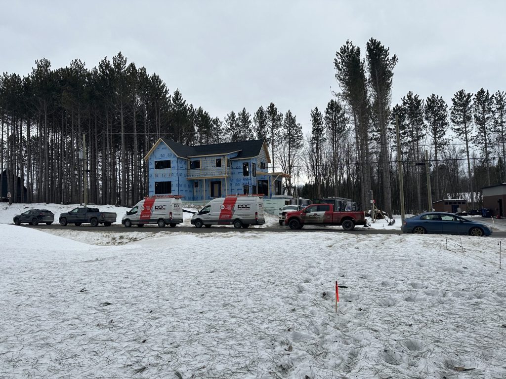 Résidence à étage enveloppée de pare-air bleu avec plusieurs véhicules Doc Électrique garés