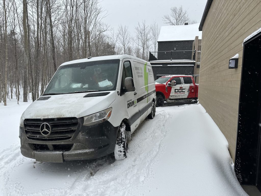 Véhicules de service Kohler et Doc Électrique stationnés près d'une résidence, en hiver