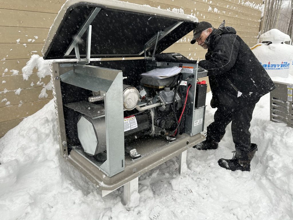 Technicien inspectant le moteur d'une génératrice Kohler résidentielle, en hiver