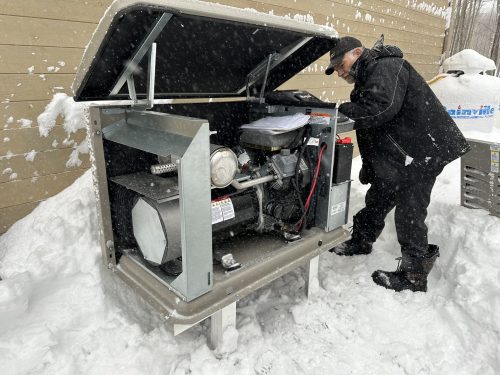 Technicien inspectant le moteur d'une génératrice Kohler résidentielle, en hiver