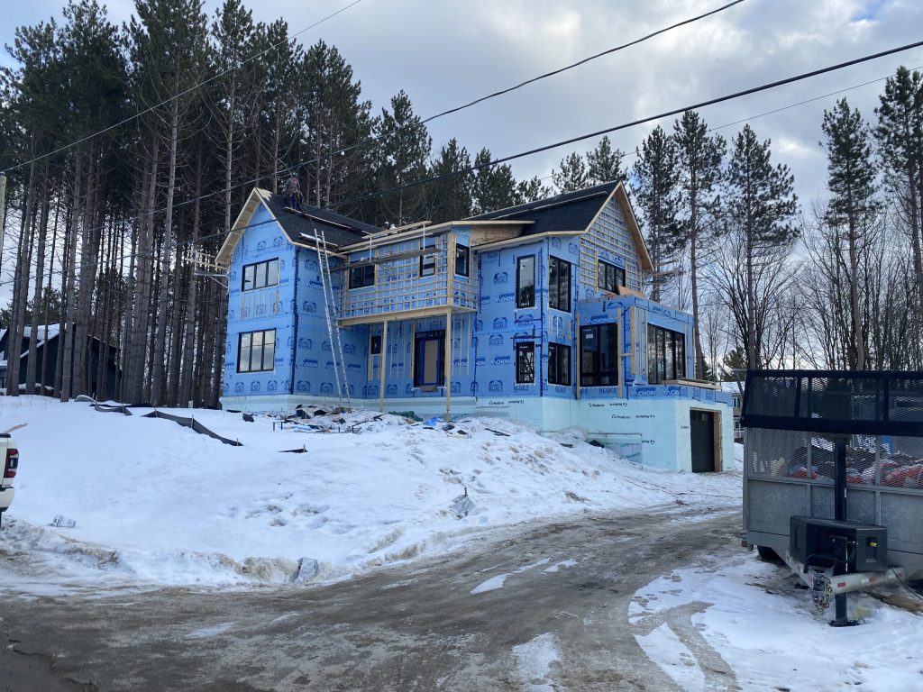 Résidence à étage en construction enveloppée de pare-air bleu, toiture en cours de pose