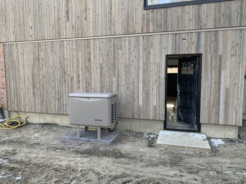 Génératrice résidentielle Kohler installée sur un socle extérieur près d'un mur en bois
