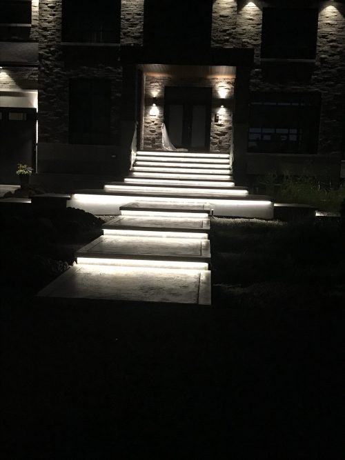 Escalier extérieur illuminé par bandeau DEL intégré devant une entrée en pierre, la nuit