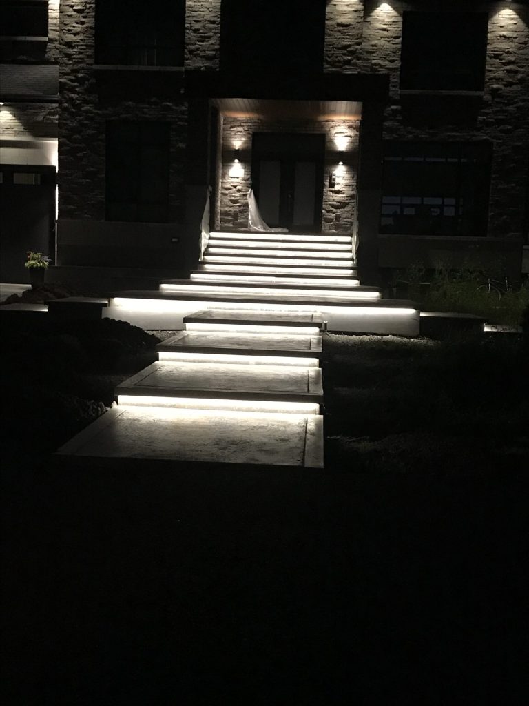Escalier extérieur illuminé par bandeau DEL intégré devant une entrée en pierre, la nuit