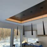 Plafond en bois avec éclairage encastré et indirect, suspensions noires au-dessus d'un îlot