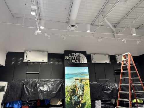 Installation de luminaires sur rail dans une boutique commerciale, échelle en place