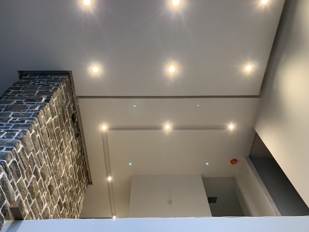 Plafond cathédrale résidentiel avec multiples spots encastrés au-dessus d'un mur de pierre