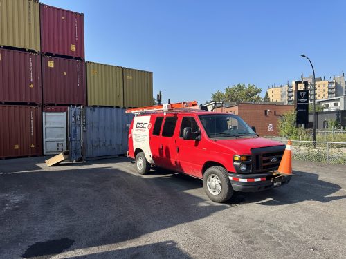 Fourgon Doc Électrique stationné près de conteneurs maritimes empilés