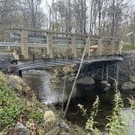Conduits électriques installés sous un pont en bois traversant un ruisseau