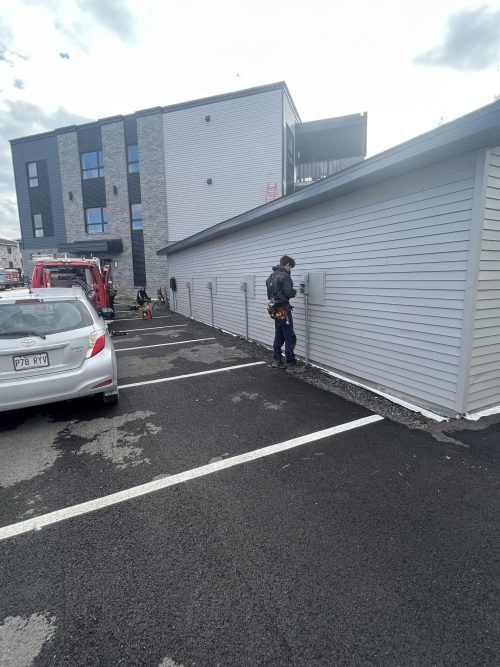 Électricien installant plusieurs bornes de recharge sur le mur extérieur d'un bâtiment résidentiel