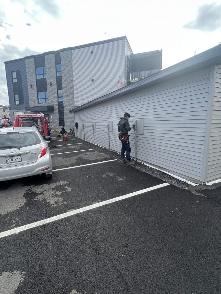 Électricien installant plusieurs bornes de recharge sur le mur extérieur d'un bâtiment résidentiel